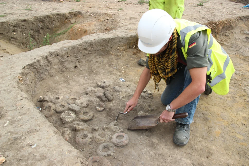 archaeologist troweling around a cache of loomweights