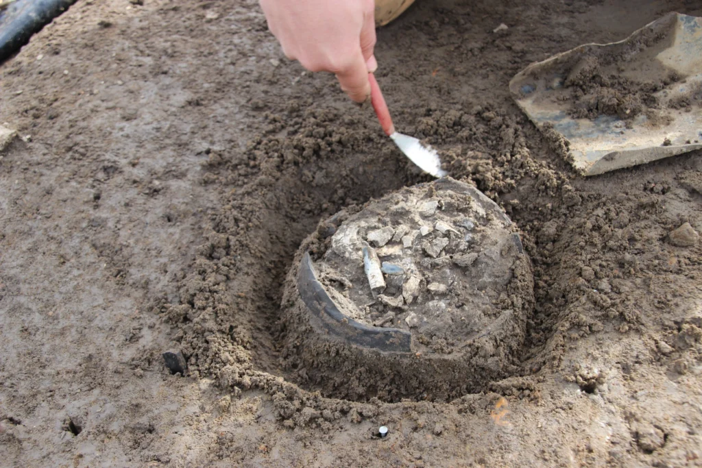 working photo of cremation excavation. The urn is partly exposed with cremated bone visible from the top.