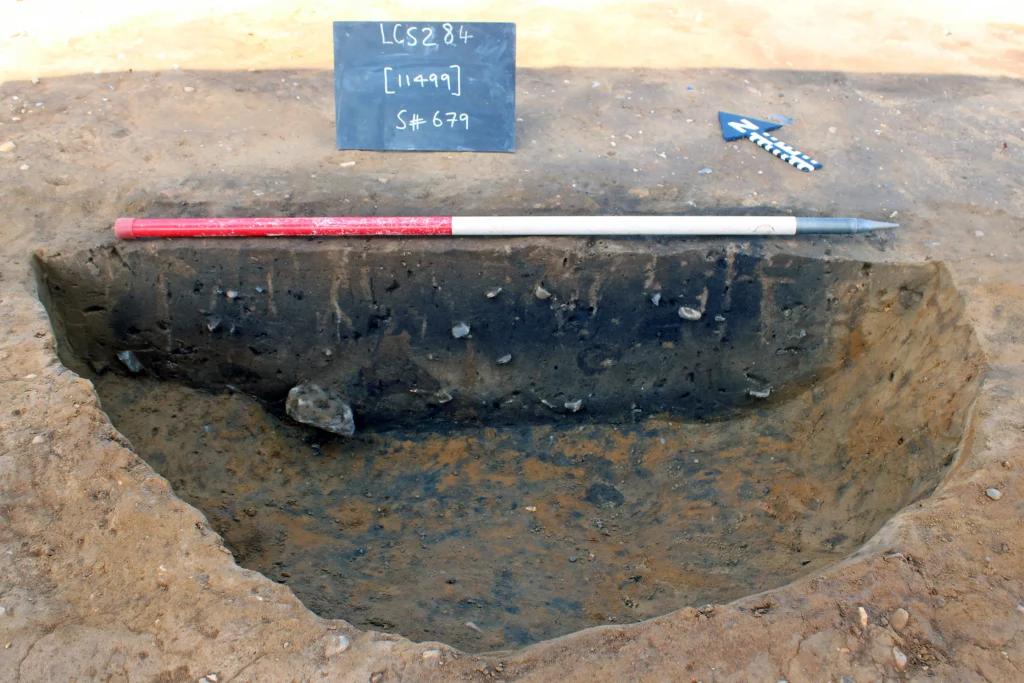 record photo of half sectioned pit, with 1m scale map north arrow and photo description board