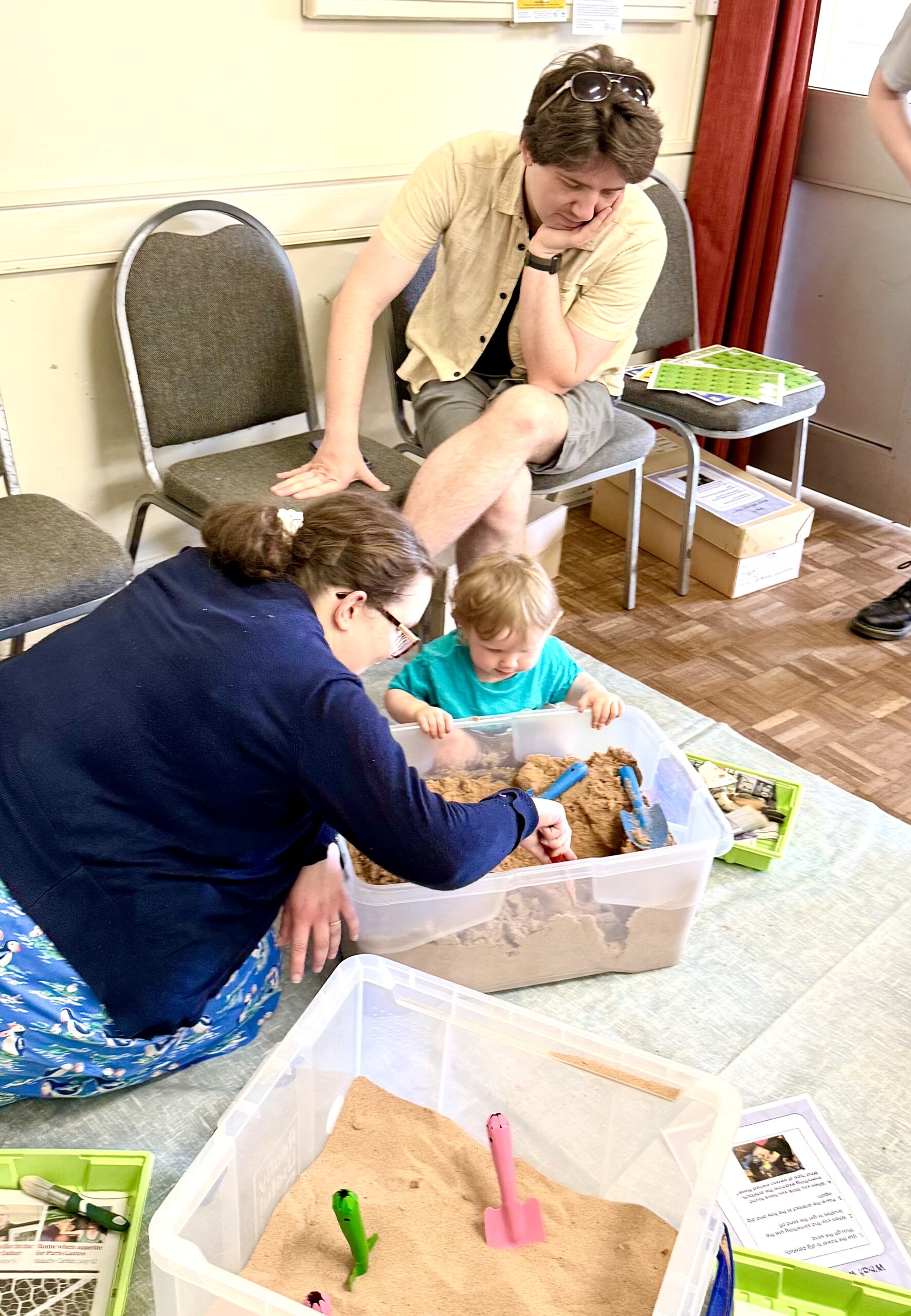 Photo of a family sat down and digging in a sand pit together