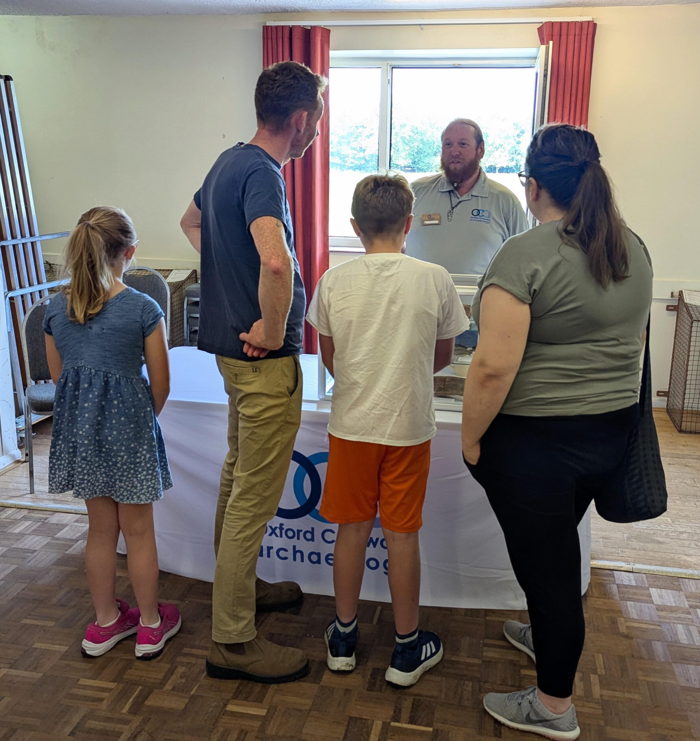 Photo of an OCA staff member standing behind a display table and speaking to a family