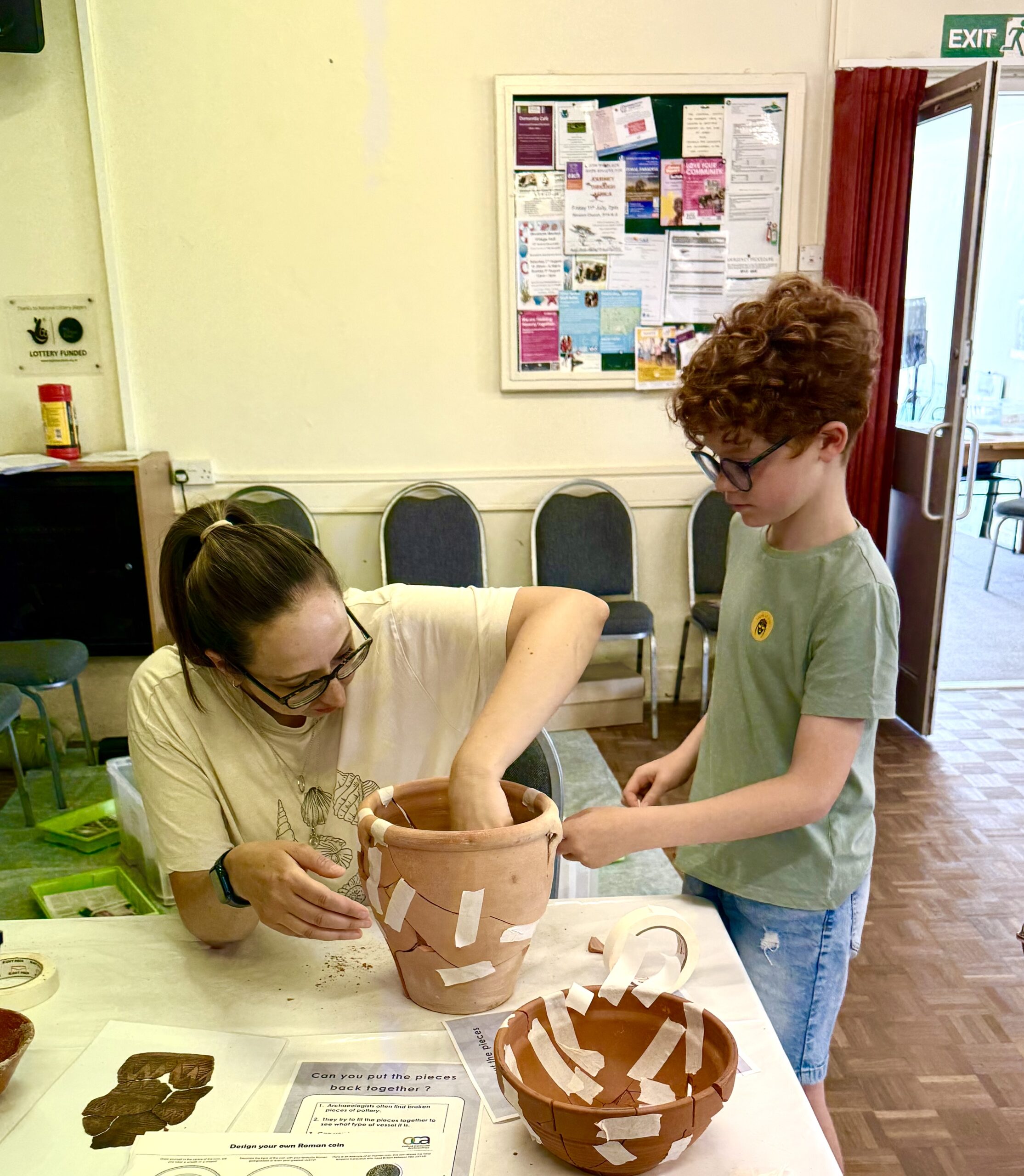 A photo of a mother and son working together to put together pieces of broken pottery