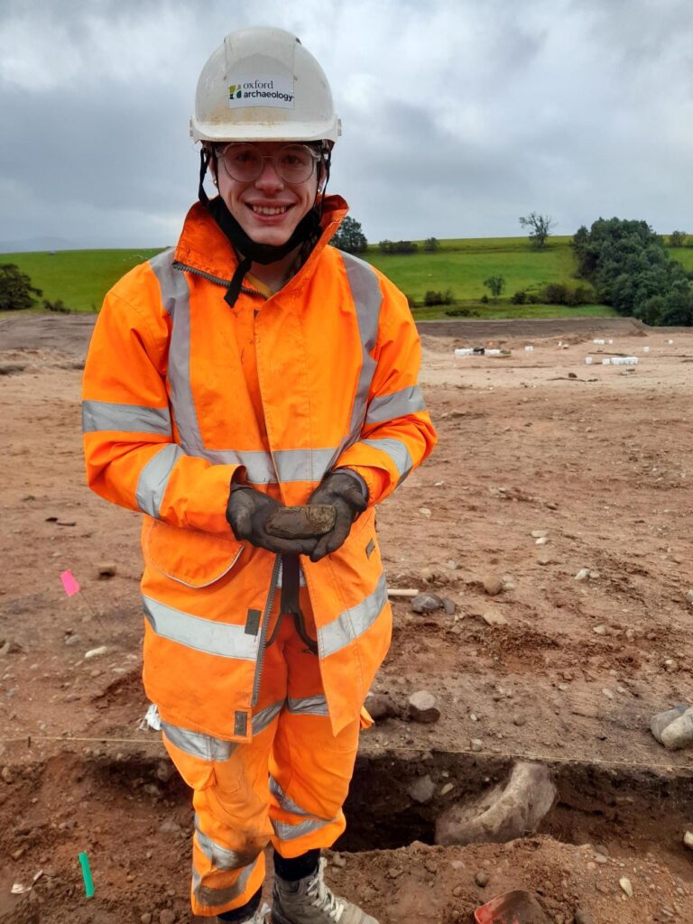 Archaeologist dressed in ppe holding stone axe, on archaeology area