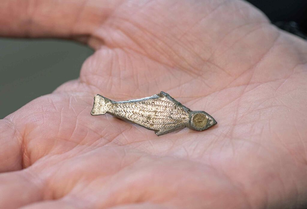 A small silver brooch that looks like a fish. It has small semi-circle impressions that resemble scales.
