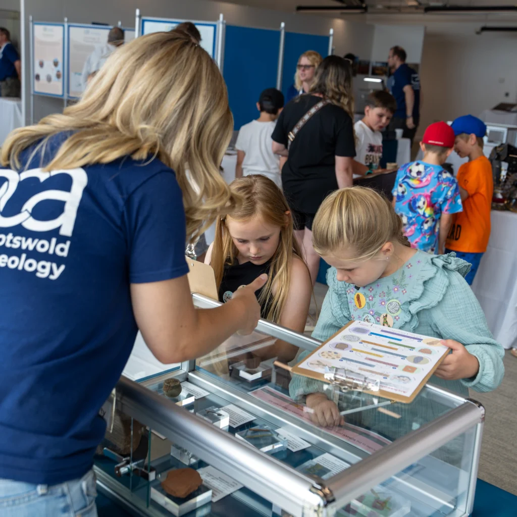 two kids look into a glass display case, one leans a clipboard with a sticker trail on the case.