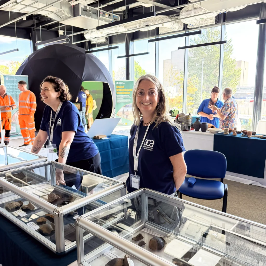 Two women in dark blue t-shirts stand behind glass display cases filled with artifacts