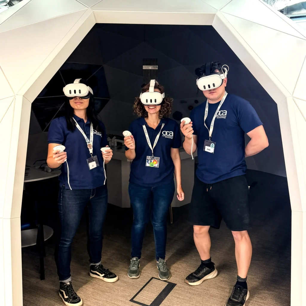 Three individuals wearing VR headsets and holding controllers stand inside a white geodesic dome structure.