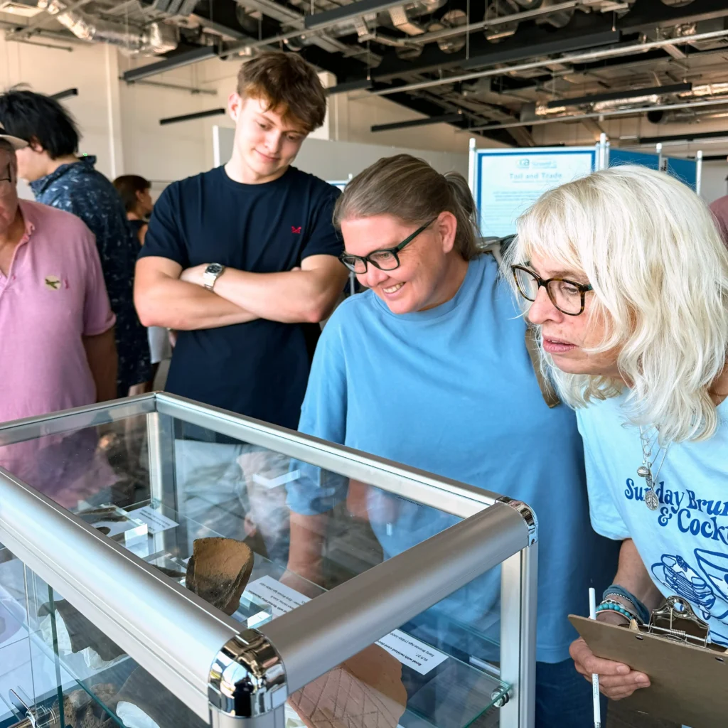Three adults and one young man examine artifacts displayed in a glass case at an exhibition.